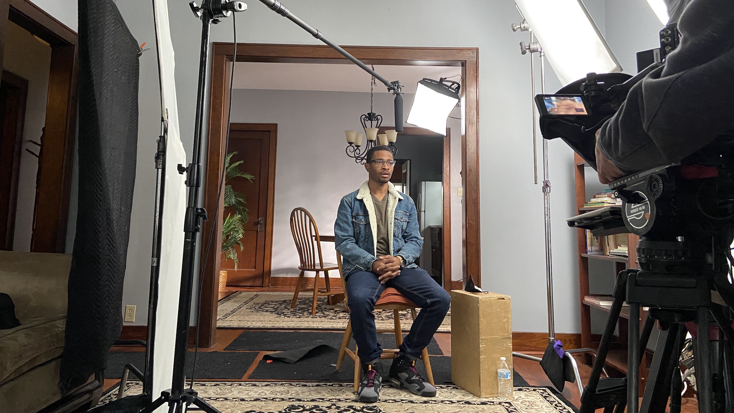 Young man sits for camera crew interview in a living room.